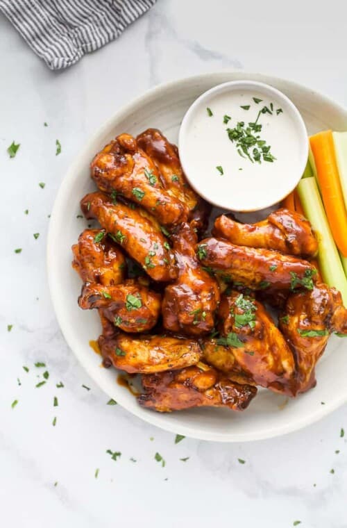 Close up overhead view of air fryer chicken wings on a white plate next to a side of crudités and ranch dressing.