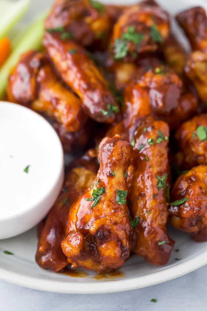Air fryer chicken wings on a white plate with a side of ranch dressing in a small bowl.