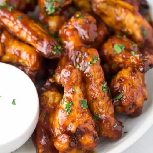 Close up of air fryer chicken wings coated with honey barbecue sauce next to a bowl of ranch dressing.