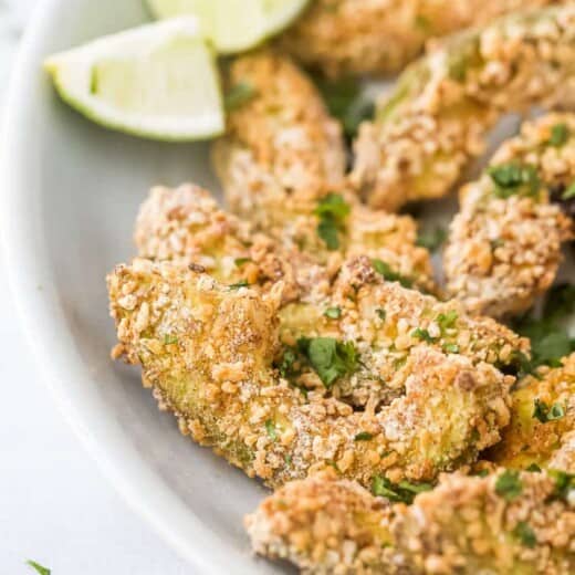 crispy avocado fries on a plate with lime wedges