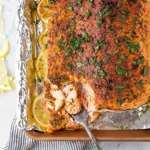 fork scooping baked salmon off of a baking sheet