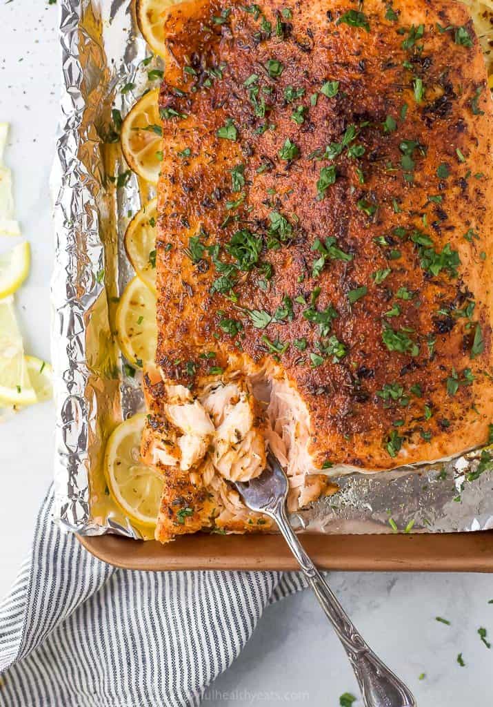 fork scooping baked salmon off of a baking sheet