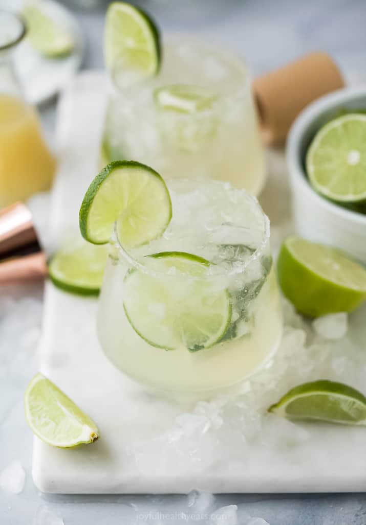 Two Margaritas on a Cutting Board with Lime Wedges and Crushed Ice