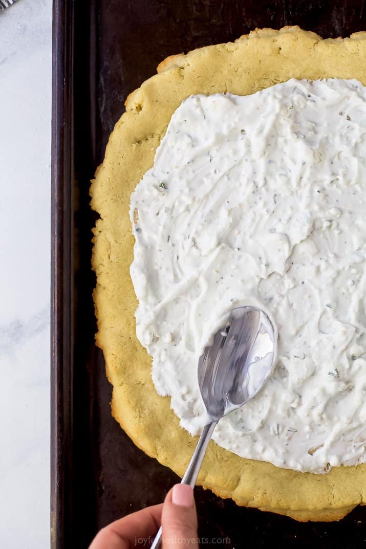 creamy gorgonzola being spread on flatbread pizza