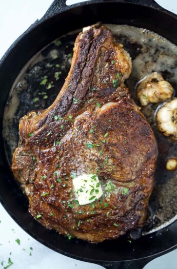 finished cowboy steak in a cast iron skillet with butter and garlic