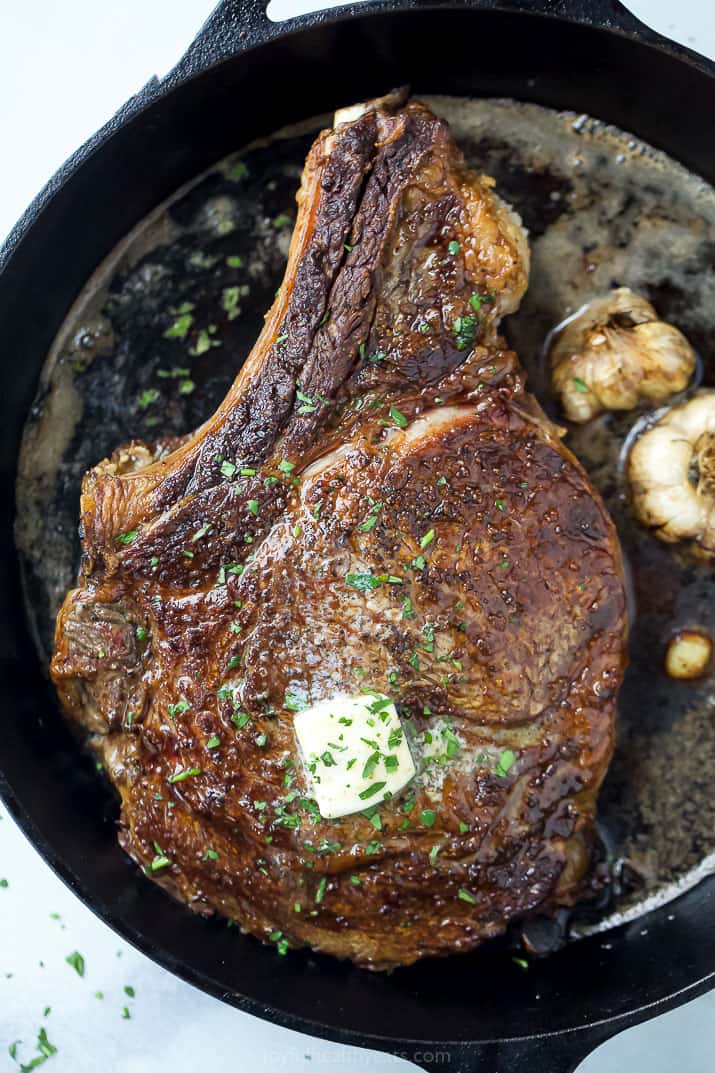 finished cowboy steak in a cast iron skillet with butter and garlic