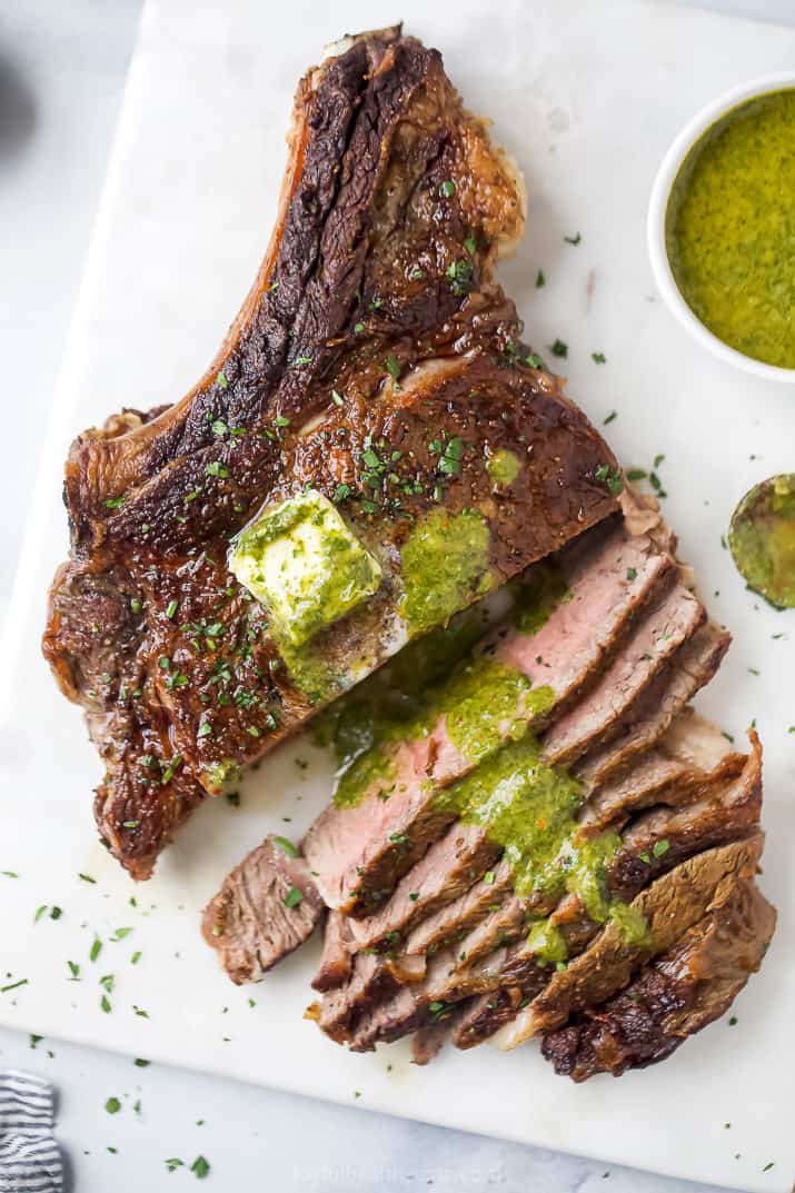 chimichurri sauce on top of a seared bone-in ribeye steak