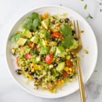 A white plate of Mexican Quinoa Salad topped with avocado and cilantro, with a gold fork.