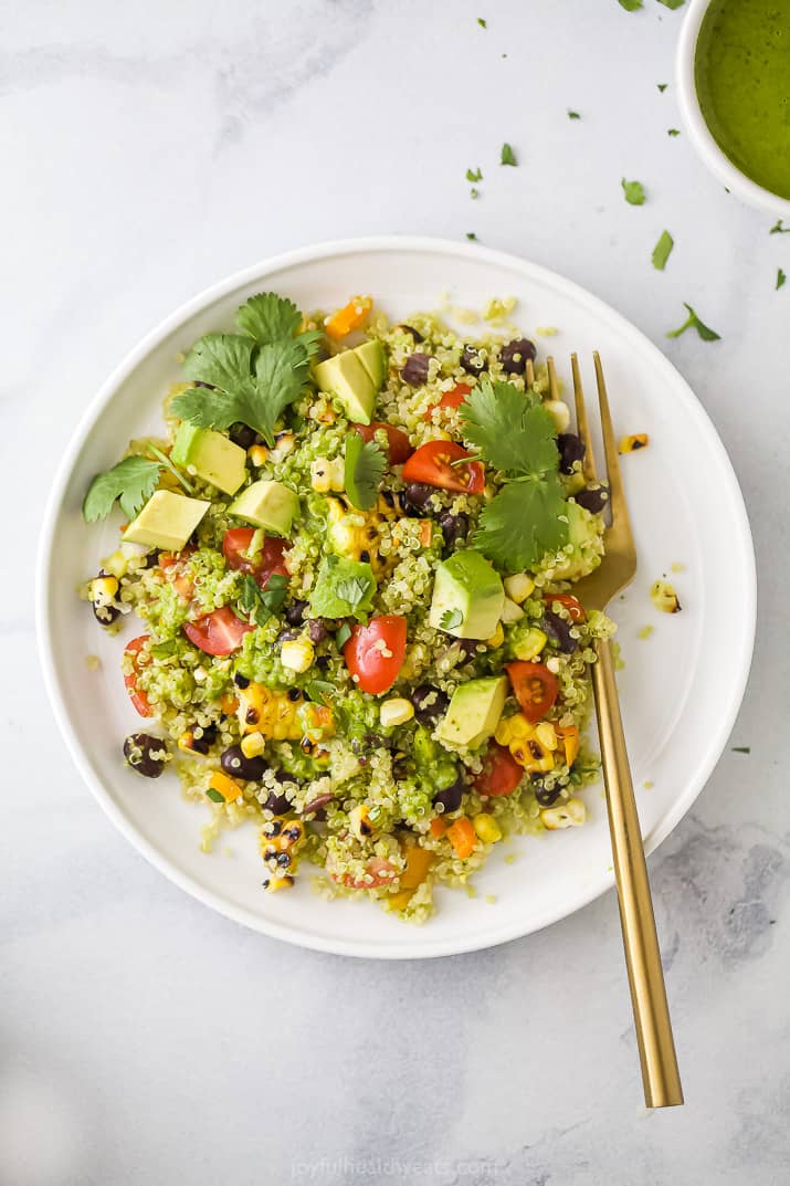 A white plate of Mexican Quinoa Salad topped with avocado and cilantro, with a gold fork.