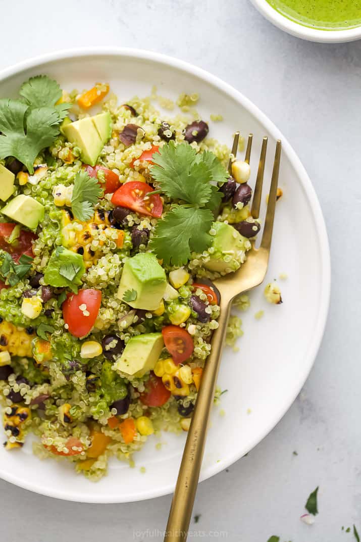 A plate of mexican quinoa salad, topped with cilantro, on a white plate with a gold fork.