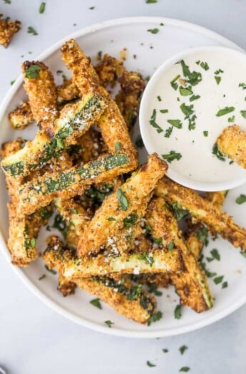 Air fryer zucchini fires on a white plate with dipping sauce