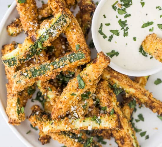 Air fryer zucchini fires on a white plate with dipping sauce