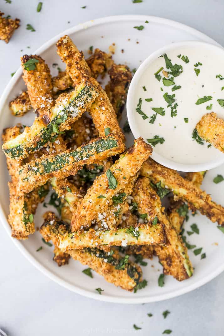 Healthy air fryer zucchini fries on a white plate with dipping sauce