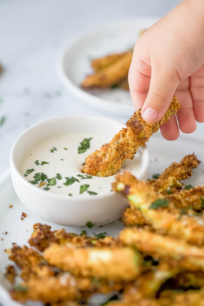 A hand dipping a zucchini fry into white aioli