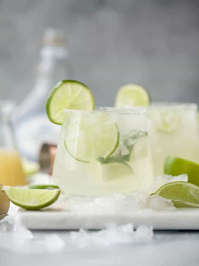 cocktail glass with a clear lime-tinted beverage and lime wedge garnish