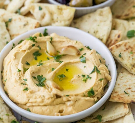 A bowl of roasted garlic hummus surrounded by pita chips and olives