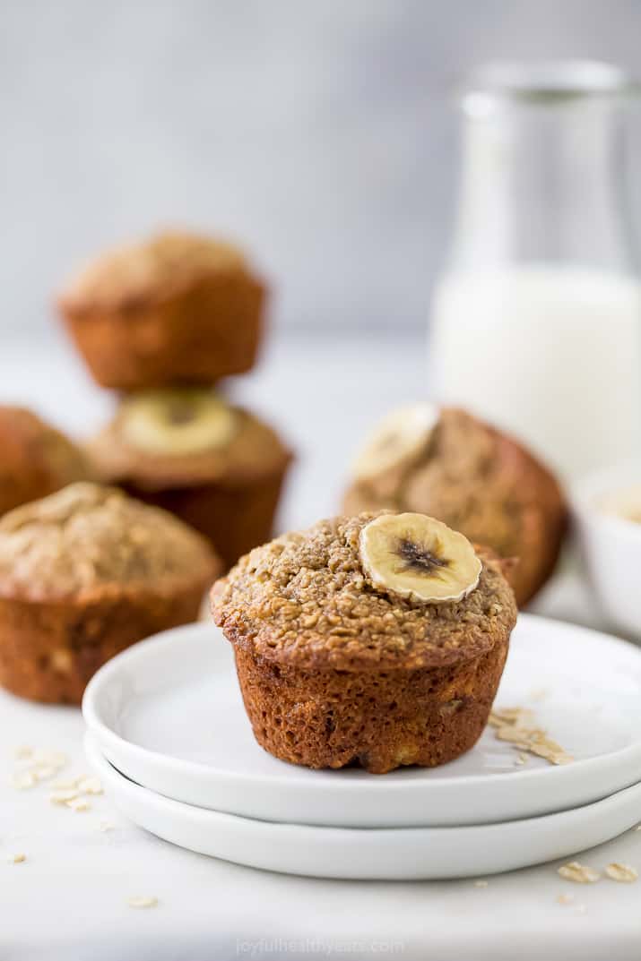 A banana muffin on a white, with more muffins and milk in the background