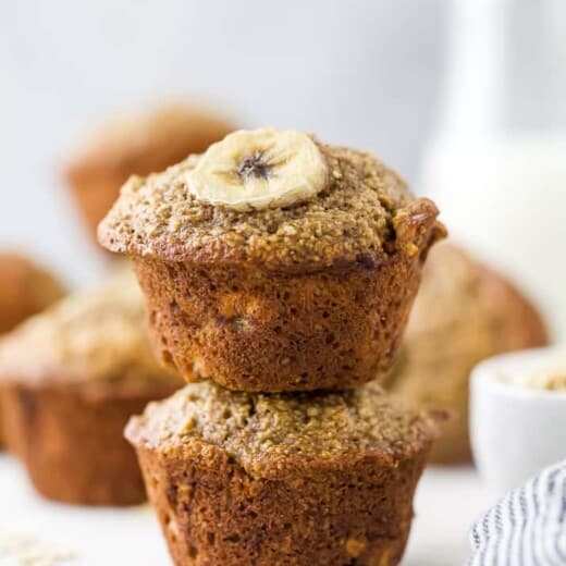 Banana oat muffins stacked on top of each other, with milk in the background