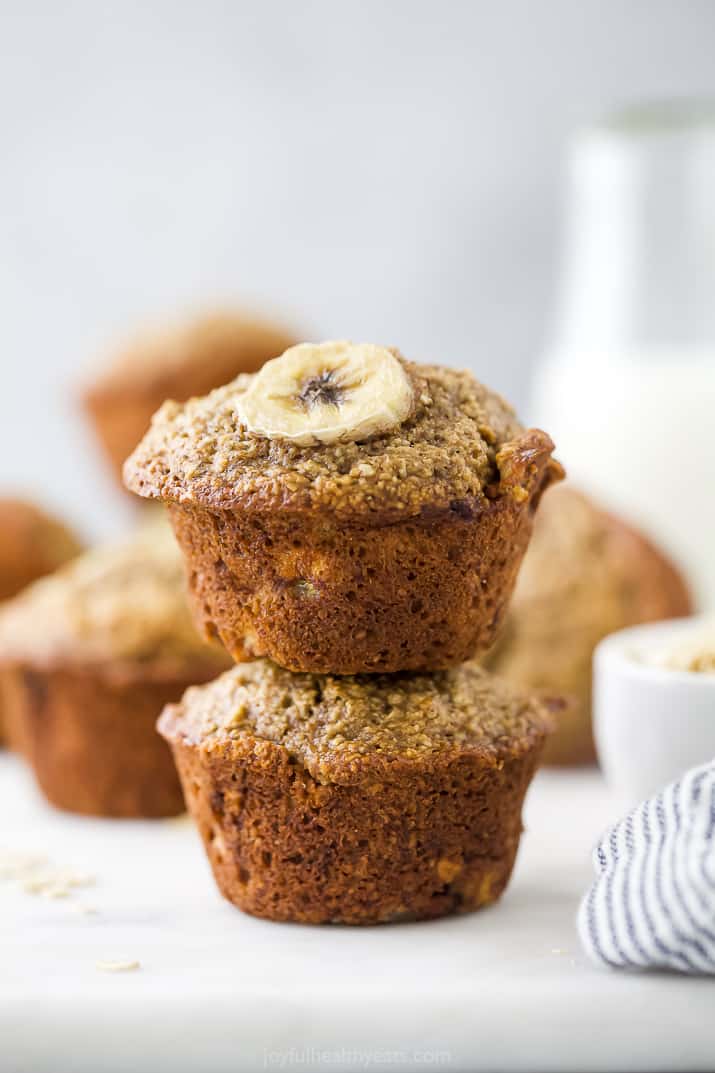 Banana oat muffins stacked on top of each other, with milk in the background