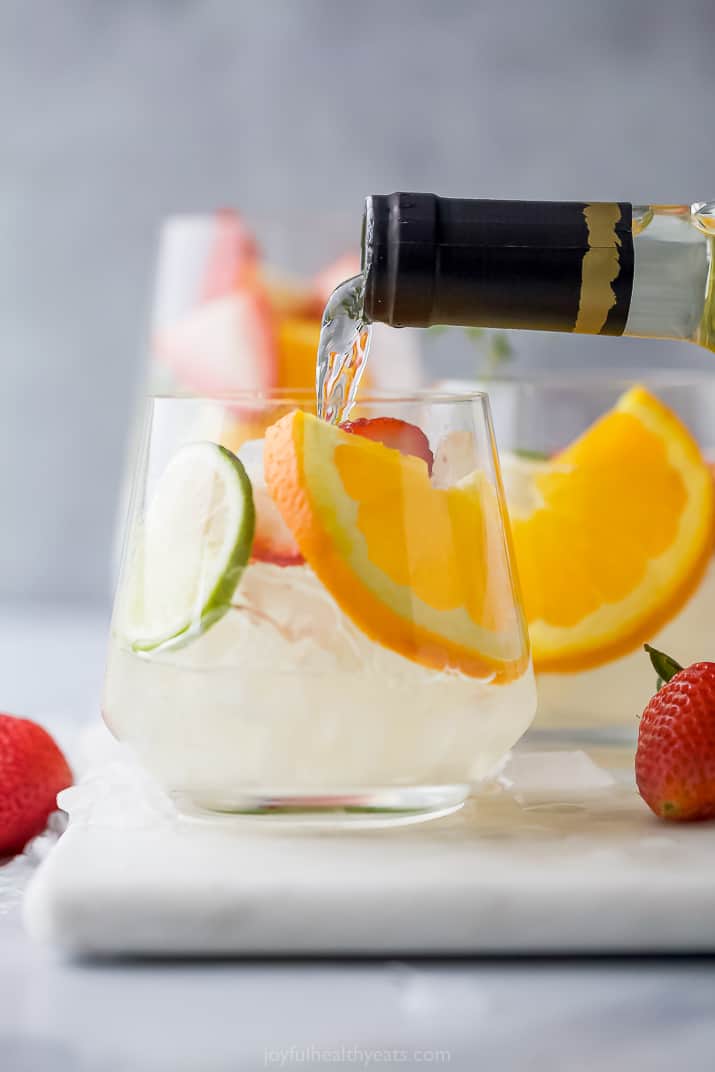 White wine being poured into a glass with ices, orange, lime and strawberry slices