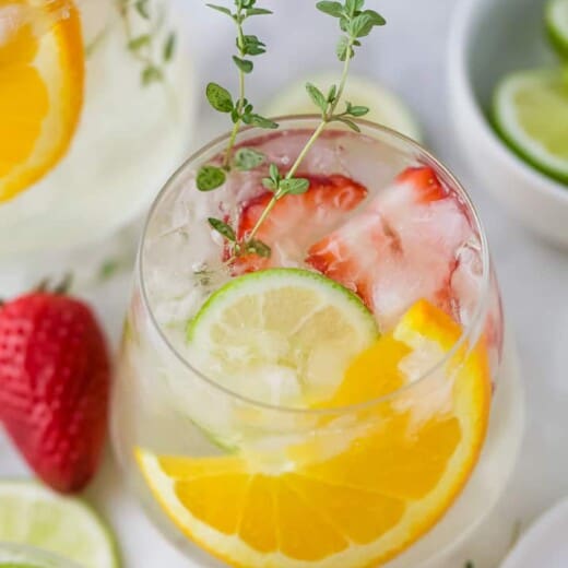 A glass of wine spritzer with strawberries, orange slices, and lime slices