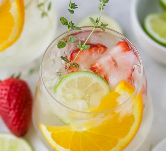 A glass of wine spritzer with strawberries, orange slices, and lime slices