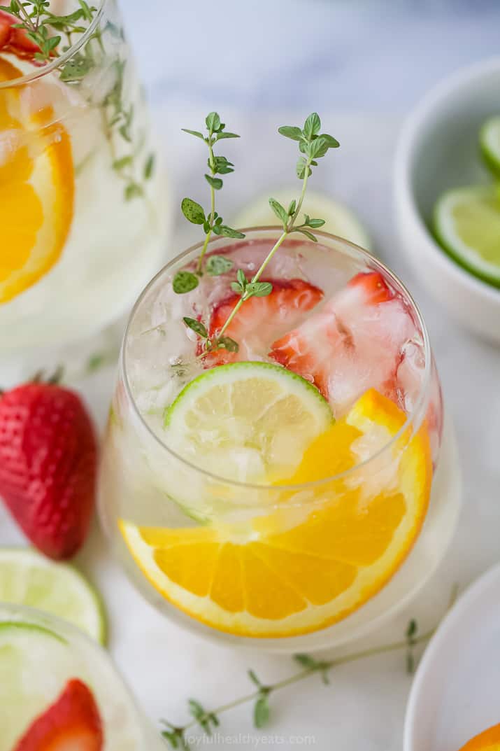 A glass of wine spritzer with strawberries, orange slices, and lime slices