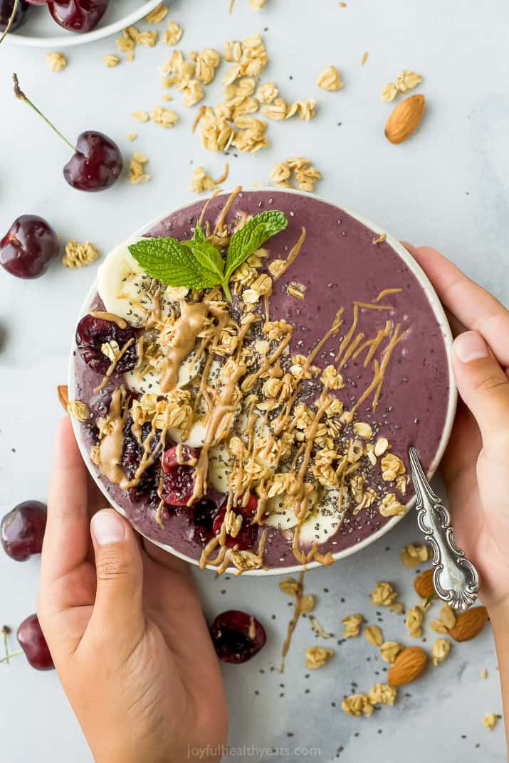 hands holding a cherry almond smoothie bowl