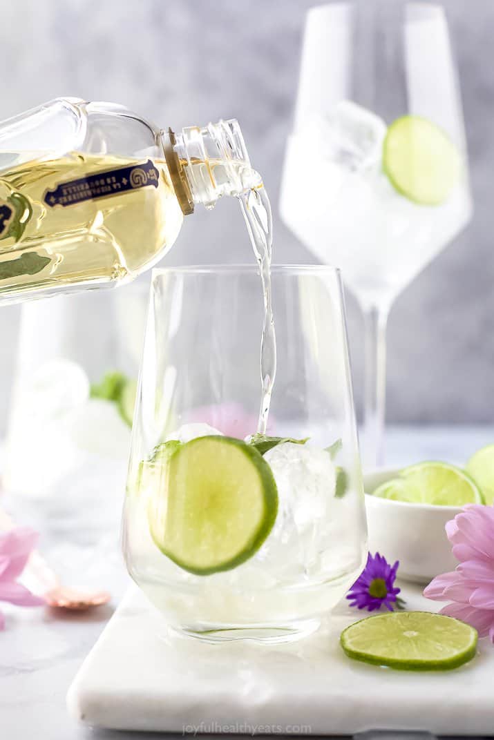 St. Germain being poured into a wine glass with ice and lime slices