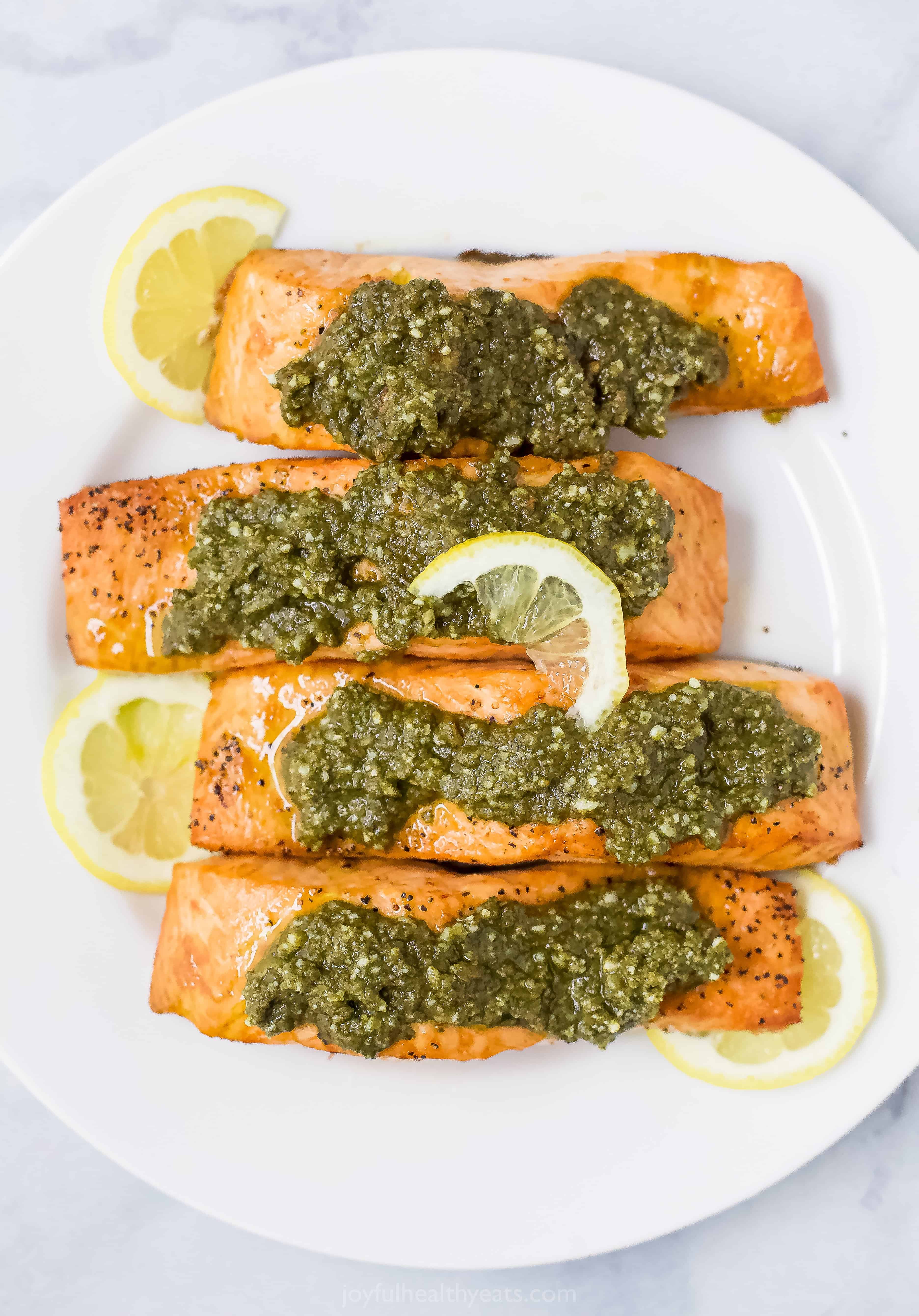 salmon filets on a plate topped with basil pesto