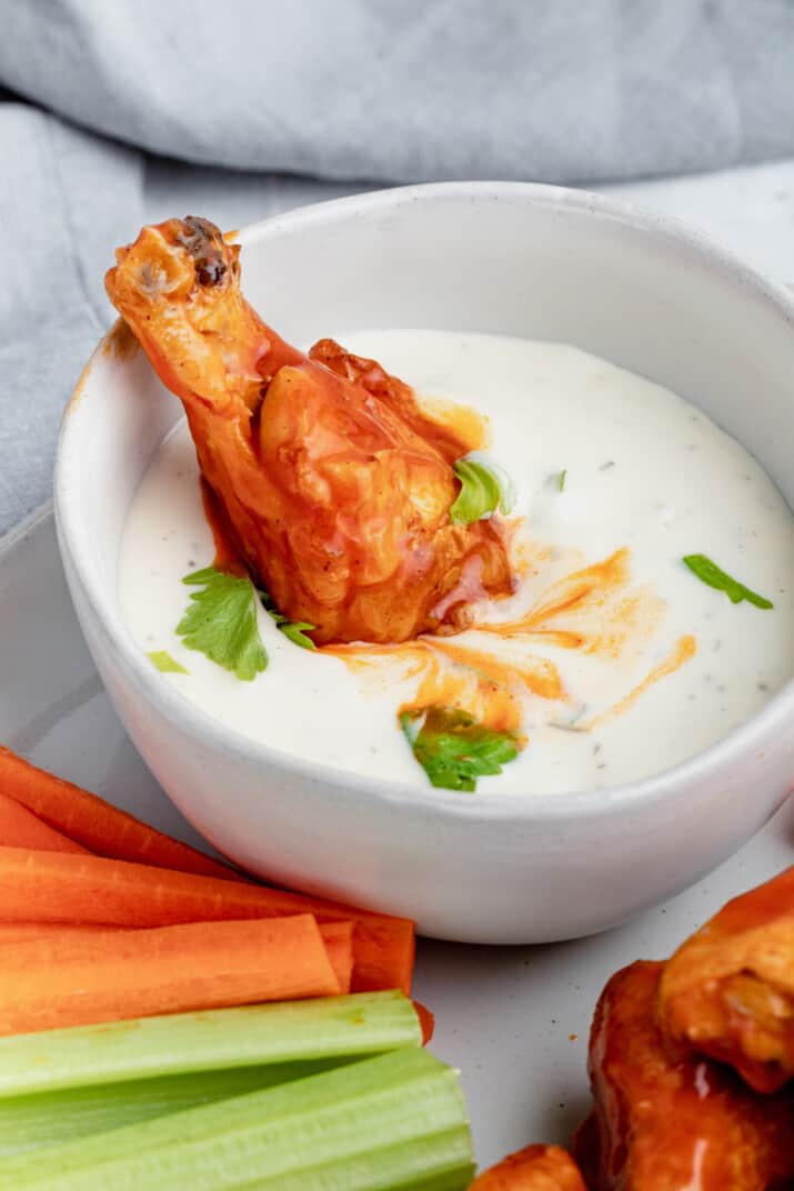A Crispy Buffalo Chicken Wing Sticking Into a Small Bowl of Ranch Dressing