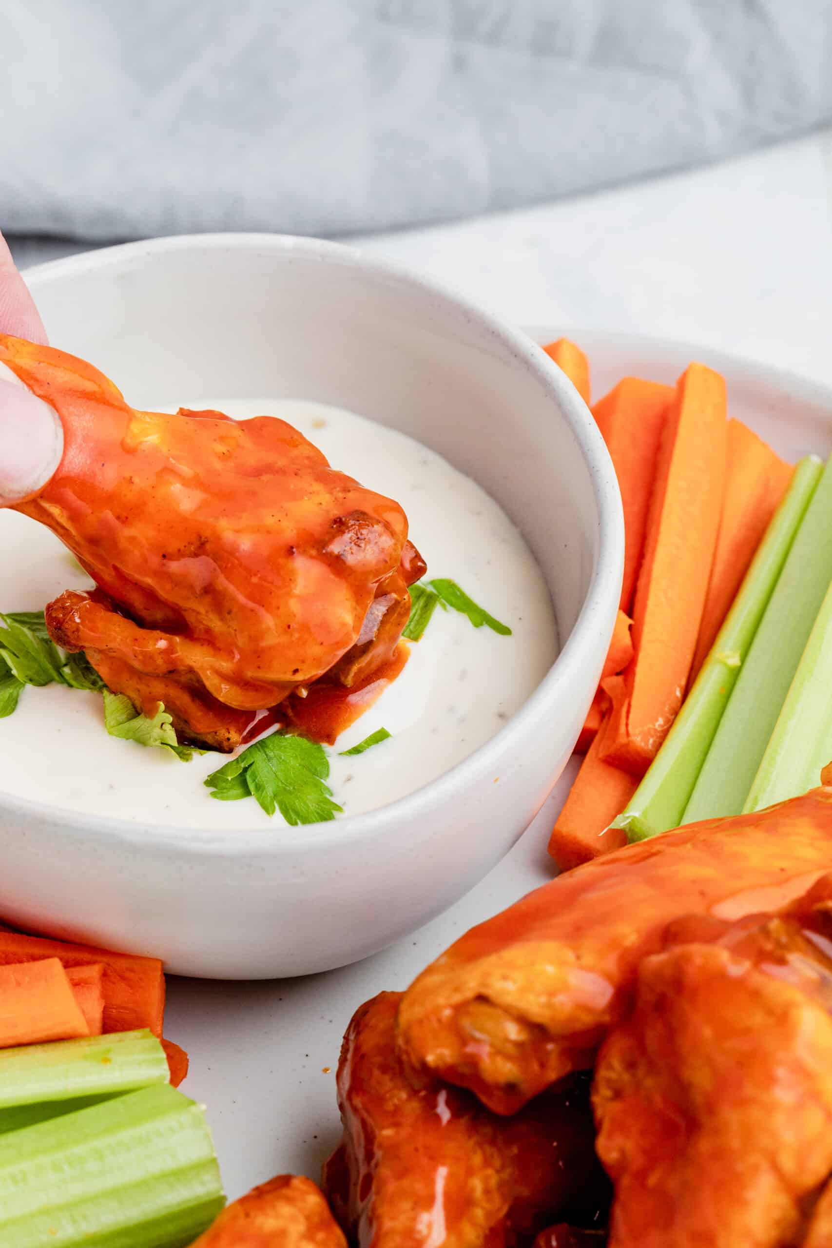 A Piece of Buffalo Chicken Being Dipped Into a Bowl of Ranch Garnished with Chopped Parsley