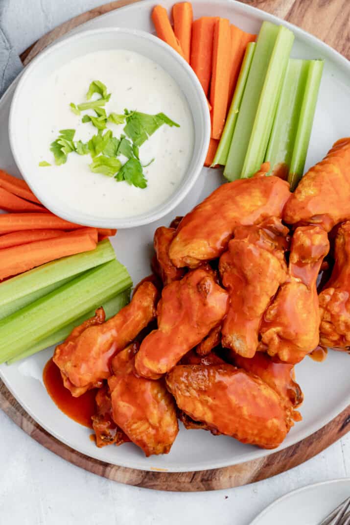 Baked Buffalo Chicken Wings Piled Onto a Plate with Raw Vegetables and Ranch Dressing