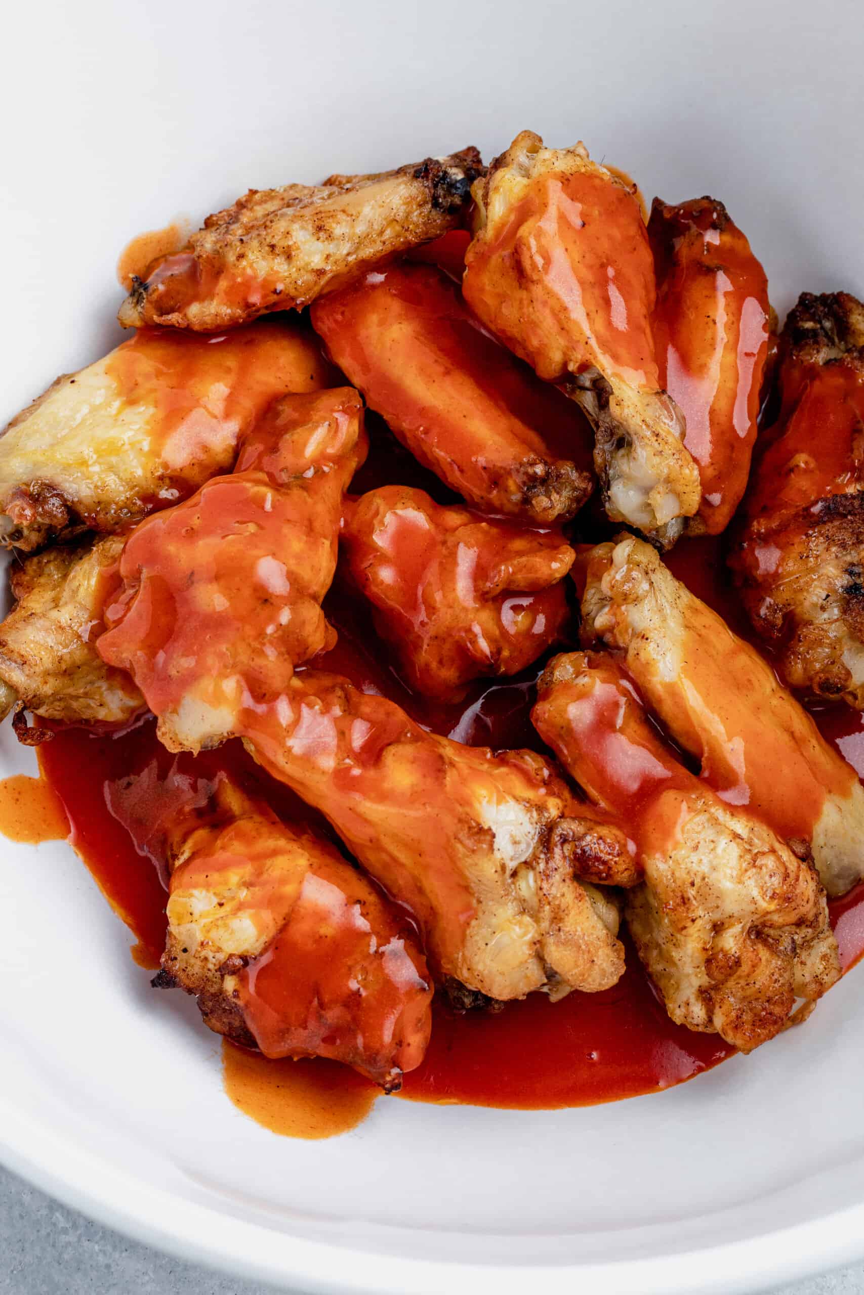 Overhead view of baked chicken wings smothered with buffalo sauce in a bowl.