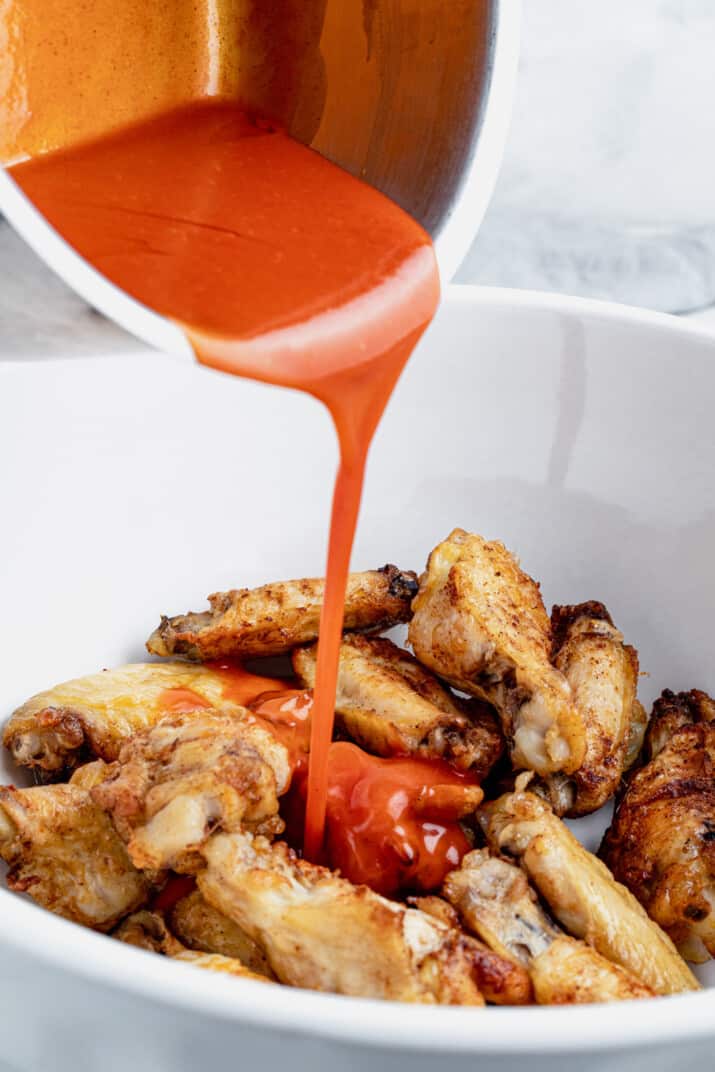 The Buffalo Sauce Mixture Being Poured Over a Bowl of Baked Chicken Wings