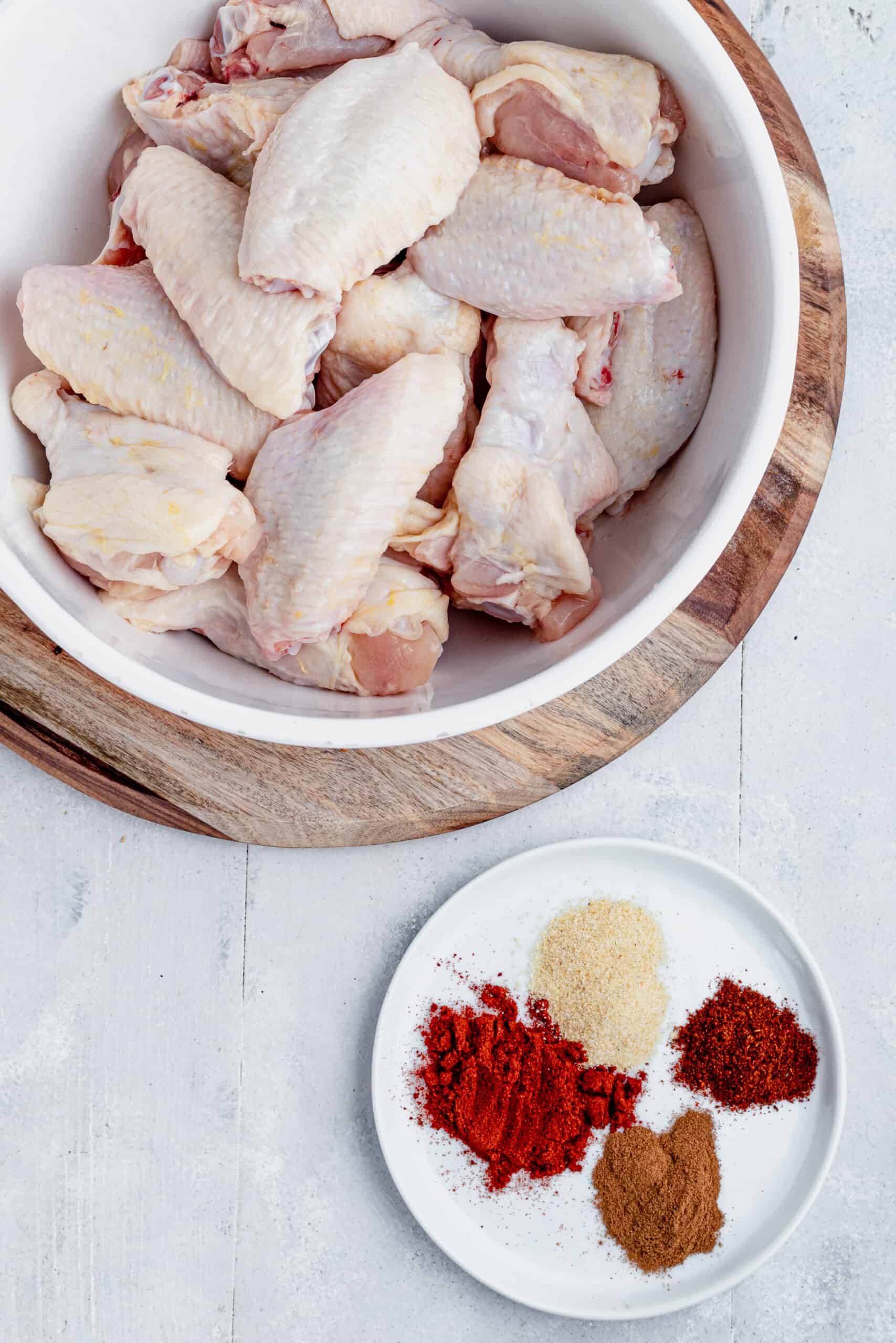 A Bowl of Raw Chicken Beside a Plate of Smoked Paprika, Cinnamon, Garlic Powder and Chipotle Chili Powder