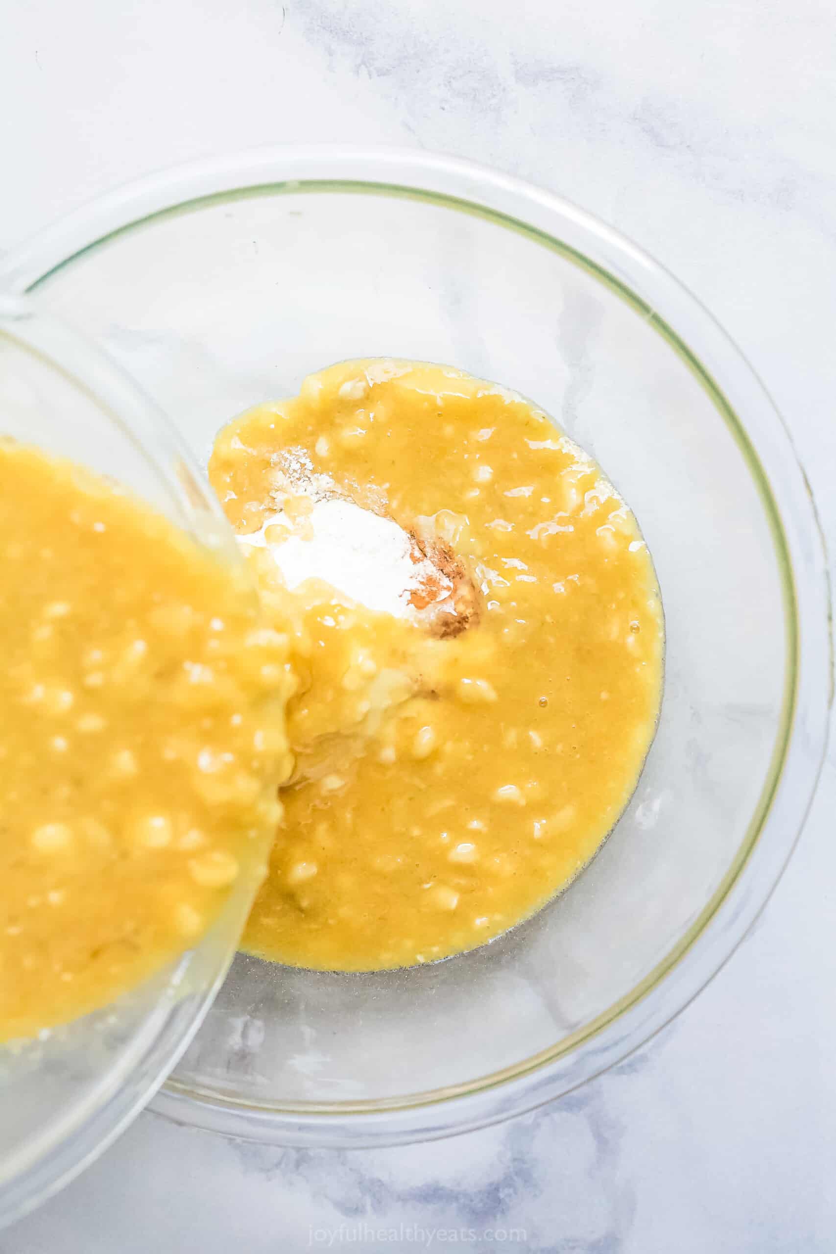 The Wet Ingredient Mixture Being Poured Over the Dry Ingredients in a Glass Bowl