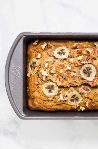 A Metal Loaf Pan Containing a Loaf of Banana Bread with Thin Slices of Banana on Top