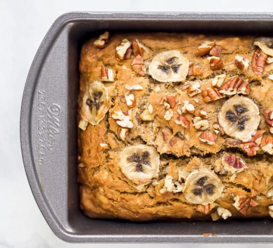 A Metal Loaf Pan Containing a Loaf of Banana Bread with Thin Slices of Banana on Top