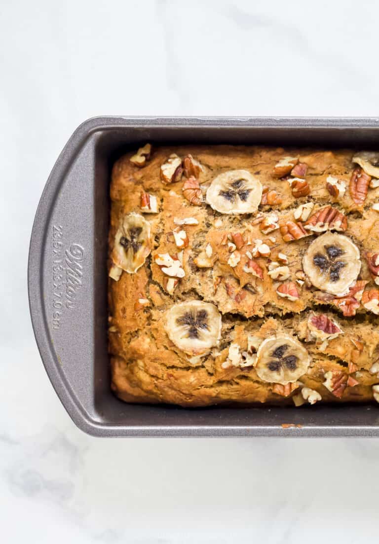 A metal loaf pan with a loaf of banana bread with thin slices of banana on top