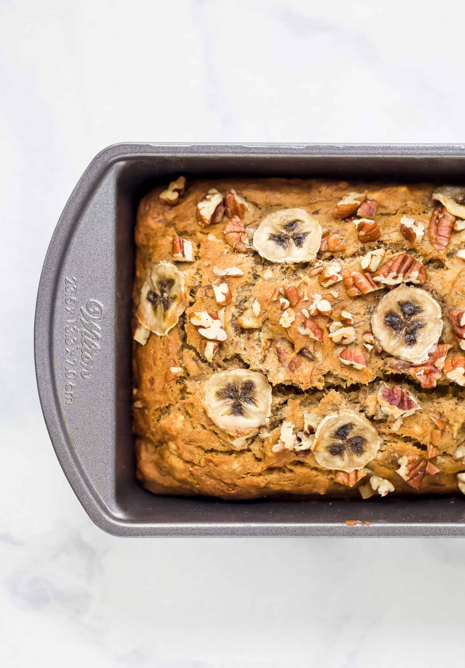 A Metal Loaf Pan Containing a Loaf of Banana Bread with Thin Slices of Banana on Top