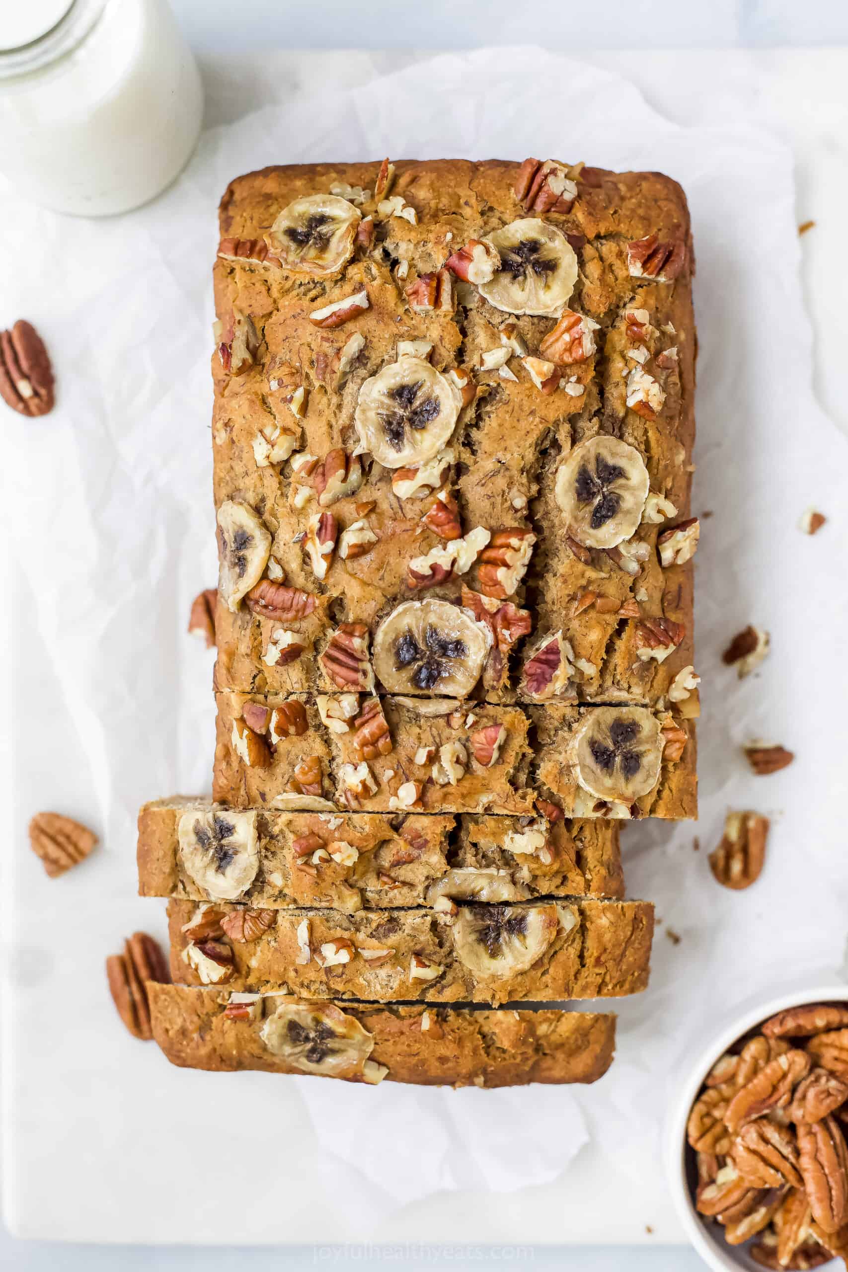 A Loaf of Banana Nut Bread Beside a Bowl of Pecans and a Glass of Milk