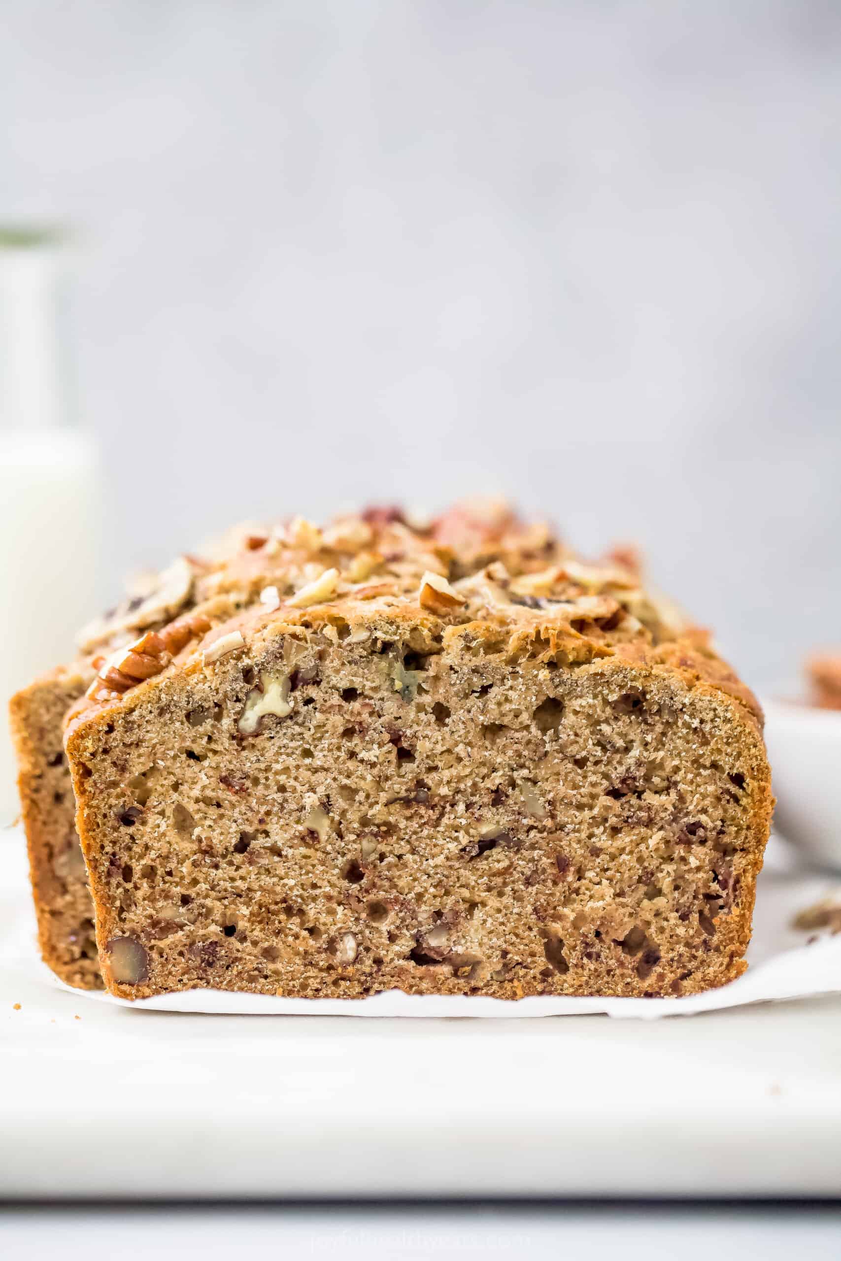 A Loaf of Banana Nut Bread on a White Surface with a Glass of Milk in the Background