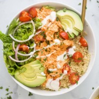 A close-up shot of a buffalo chicken quinoa bowl topped with chopped cilantro and ranch dressing