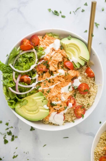 A close-up shot of a buffalo chicken quinoa bowl topped with chopped cilantro and ranch dressing