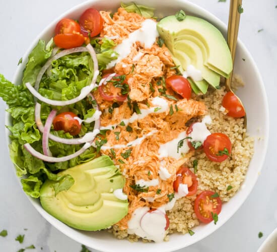 A close-up shot of a buffalo chicken quinoa bowl topped with chopped cilantro and ranch dressing