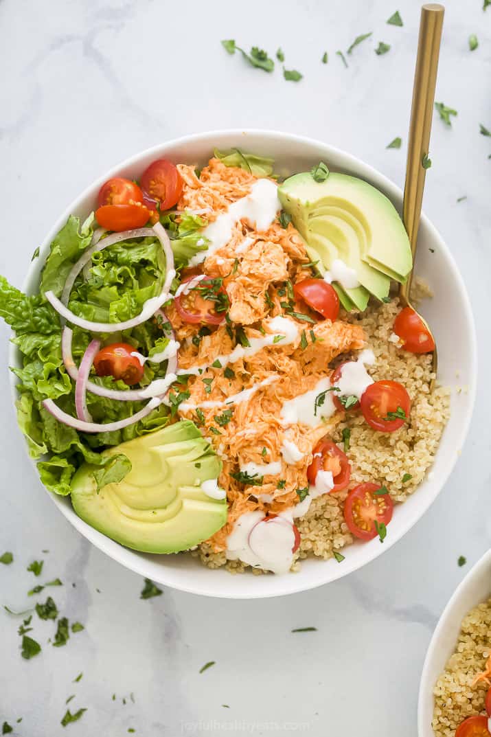 A close-up shot of a buffalo chicken quinoa bowl topped with chopped cilantro and ranch dressing