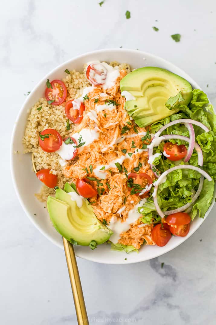 A buffalo chicken quinoa bowl on a granite surface with a golden spoon inside