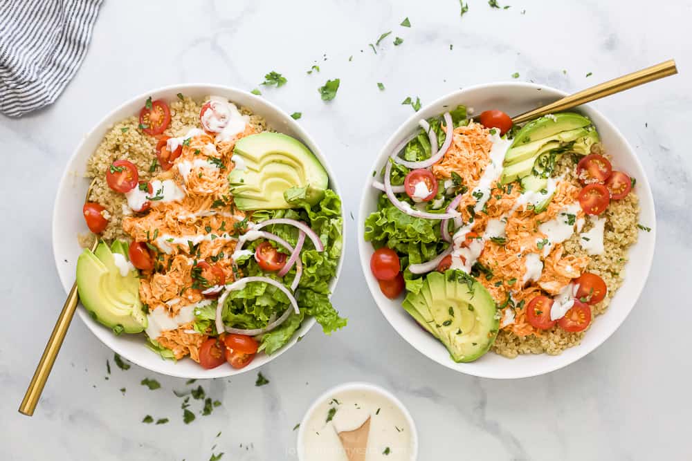 Two buffalo chicken quinoa bowls on a countertop with a small bowl of ranch dressing