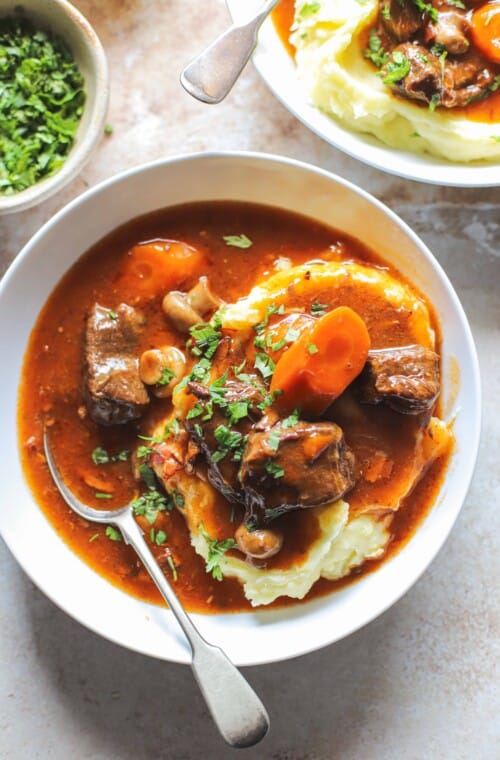 close up of beef bourguignon in a bowl over mashed potatoes